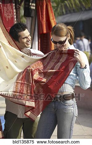Stock Photography - Couple admiring fabrics at outdoor market. Fotosearch