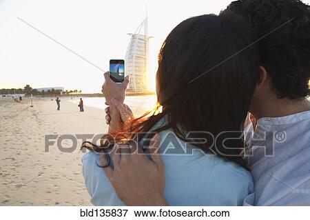 Couple taking pictures together on beach, Dubai, United Arab Emirates View Large Photo Image Stock Photo - Couple taking pictures together on beach, Dubai, United Arab Emirates. Fotosearch