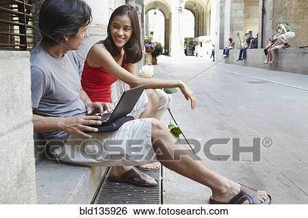 Stock Photograph - Couple using laptop on city street. Fotosearch