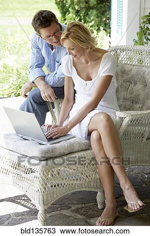 Stock Image - Couple using laptop together on patio. Fotosearch