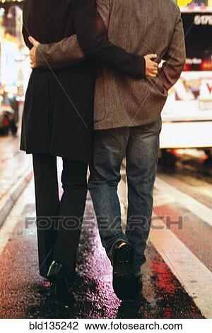 Stock Image - Couple walking on city street lit up at night. Fotosearch