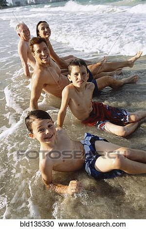 Stock Image - Family sitting in waves on beach. Fotosearch