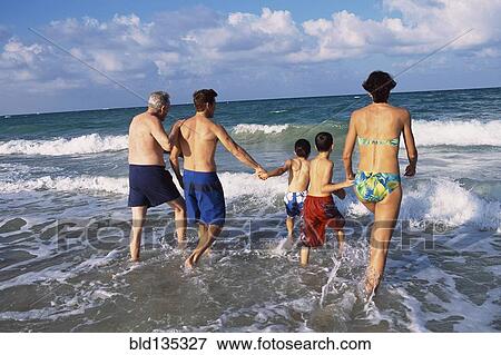 Stock Photo - Family walking in waves on beach. Fotosearch