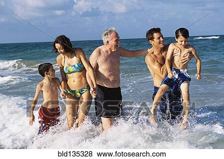 Stock Photo - Family walking in waves on beach. Fotosearch
