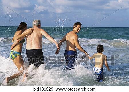 Stock Photo - Family walking in waves on beach. Fotosearch