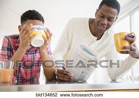 Stock Image - Father and son having breakfast in kitchen. Fotosearch