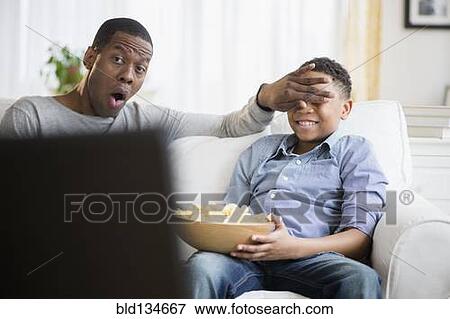 Father and son watching television on sofa View Large Photo Image Stock Photo - Father and son watching television on sofa. Fotosearch