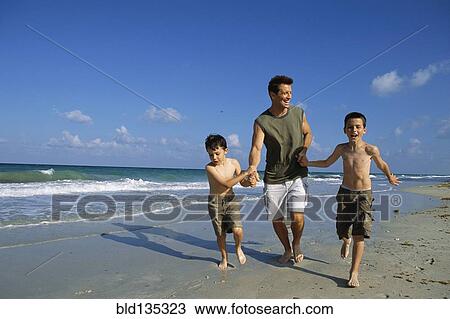 Stock Image - Father and sons walking together on beach. Fotosearch