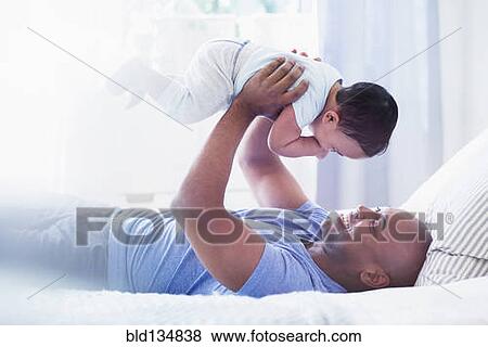 Stock Photo - Father playing with baby on bed. Fotosearch