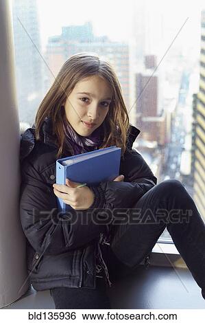 Stock Photograph - Girl holding binder on windowsill. Fotosearch