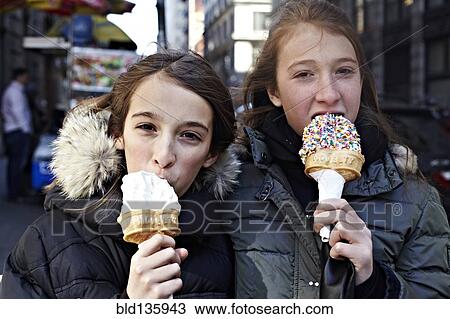 Stock Image - Girls eating ice cream on city street. Fotosearch