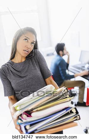 Stock Photo - Hispanic businesswoman carrying stack of folders in office. Fotosearch