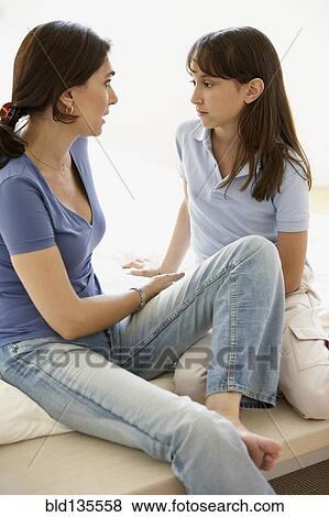 Stock Photo - Hispanic mother and daughter sitting on sofa. Fotosearch