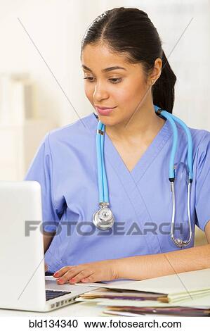 Hispanic nurse using laptop at desk View Large Photo Image Stock Image - Hispanic nurse using laptop at desk. Fotosearch