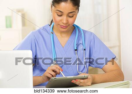 Stock Photo - Hispanic nurse using tablet computer at desk. Fotosearch