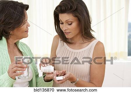 Stock Image - Hispanic woman giving mother medicine. Fotosearch