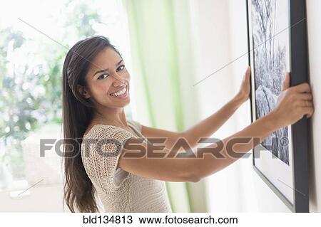 Hispanic woman hanging picture in living room View Large Photo Image Stock Image - Hispanic woman hanging picture in living room. Fotosearch