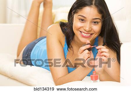 Hispanic woman painting her nails on sofa View Large Photo Image Stock Photo - Hispanic woman painting her nails on sofa. Fotosearch