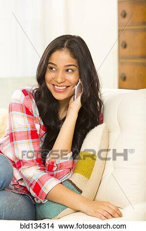 Hispanic woman talking on cell phone on sofa View Large Photo Image Picture - Hispanic woman talking on cell phone on sofa. Fotosearch