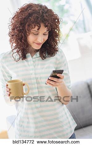 Stock Image - Hispanic woman using cell phone in living room. Fotosearch