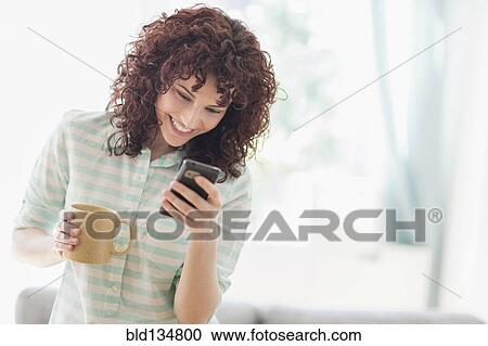 Stock Image - Hispanic woman using cell phone in living room. Fotosearch