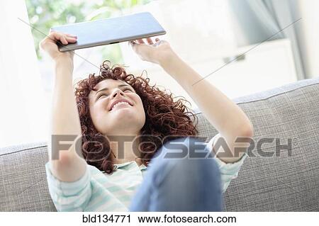 Stock Image - Hispanic woman using digital tablet on sofa. Fotosearch
