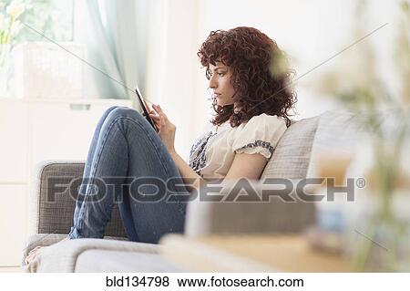 Stock Photo - Hispanic woman using digital tablet on sofa. Fotosearch