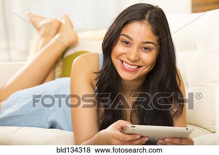 Stock Photo - Hispanic woman using tablet computer on sofa. Fotosearch