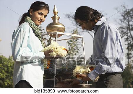 Stock Image - Indian couple offering flowers to shrine. Fotosearch