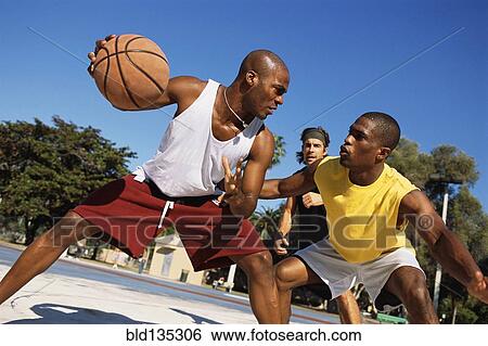 Stock Photograph - Men playing basketball outdoors. Fotosearch