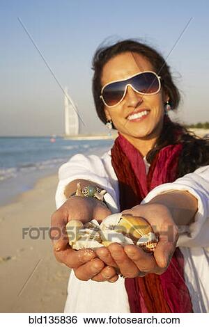Middle Eastern woman holding seashells on beach, Dubai, United Arab Emirates View Large Photo Image Stock Photograph - Middle Eastern woman holding seashells on beach, Dubai, United Arab Emirates. Fotosearch