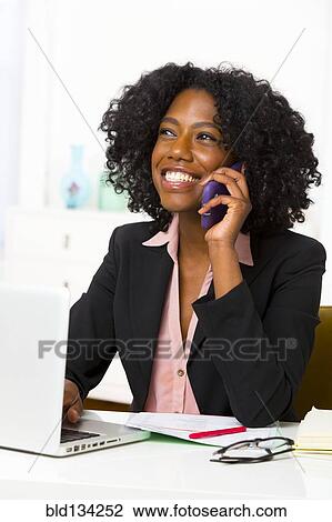 Mixed race businesswoman talking at cell phone at desk View Large Photo Image Stock Image - Mixed race businesswoman talking at cell phone at desk. Fotosearch