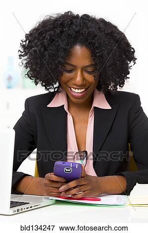 Stock Photo - Mixed race businesswoman using cell phone at desk. Fotosearch