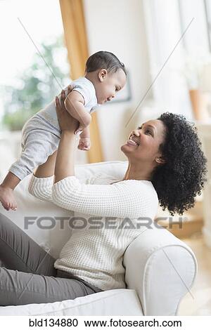 Stock Image - Mixed race mother playing with baby on sofa. Fotosearch