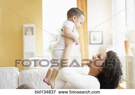 Stock Photo - Mixed race mother playing with baby on sofa. Fotosearch