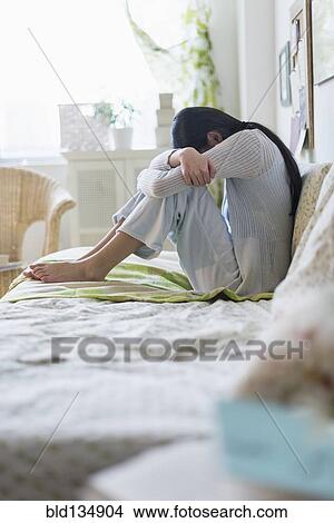 Mixed race teenage girl hugging her knees on bed View Large Photo Image Picture - Mixed race teenage girl hugging her knees on bed. Fotosearch