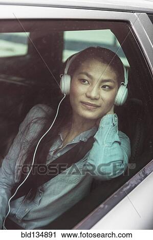 Stock Image - Mixed race teenage girl listening to headphones in backseat of car. Fotosearch