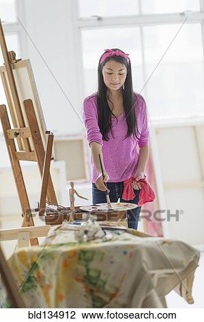 Stock Image - Mixed race teenage girl painting in studio. Fotosearch