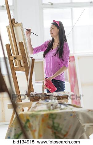 Stock Photography - Mixed race teenage girl painting in studio. Fotosearch