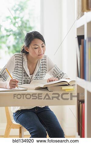 Stock Image - Mixed race teenage girl studying in library. Fotosearch