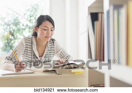 Stock Image - Mixed race teenage girl studying in library. Fotosearch