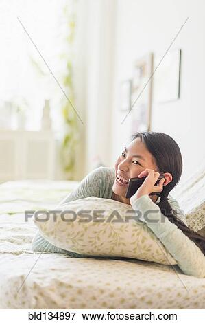 Stock Photo - Mixed race teenage girl talking on cell phone on bed. Fotosearch