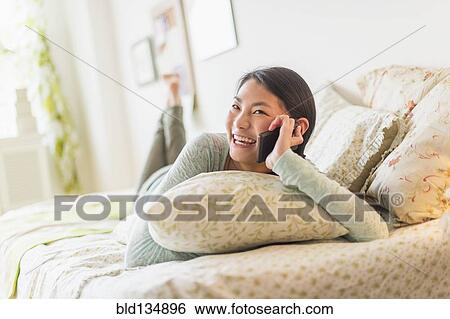 Mixed race teenage girl talking on cell phone on bed View Large Photo Image Stock Photograph - Mixed race teenage girl talking on cell phone on bed. Fotosearch