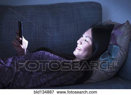 Stock Photo - Mixed race teenage girl using cell phone on sofa. Fotosearch
