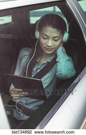 Stock Image - Mixed race teenage girl using digital tablet in backseat of car. Fotosearch