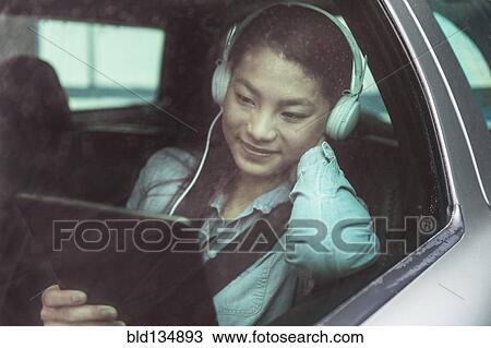 Stock Image - Mixed race teenage girl using digital tablet in backseat of car. Fotosearch