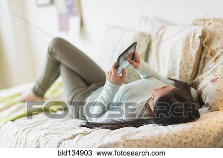 Stock Image - Mixed race teenage girl using digital tablet on bed. Fotosearch
