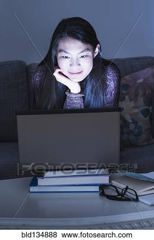 Stock Photo - Mixed race teenage girl using laptop on sofa. Fotosearch