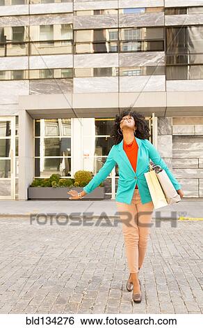 Stock Photograph - Mixed race woman carrying shopping bags on city street. Fotosearch