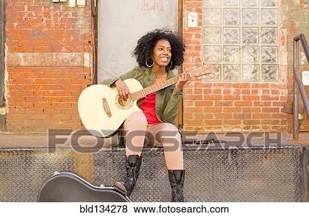 Mixed race woman playing guitar in city View Large Photo Image Stock Photo - Mixed race woman playing guitar in city. Fotosearch